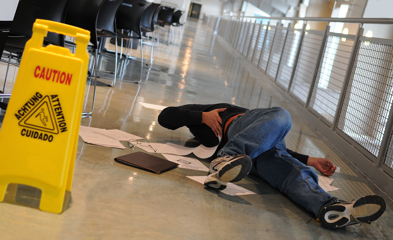 A man who slipped on a wet floor beside a bright yellow caution sign holds his back in pain, slip and fall injury