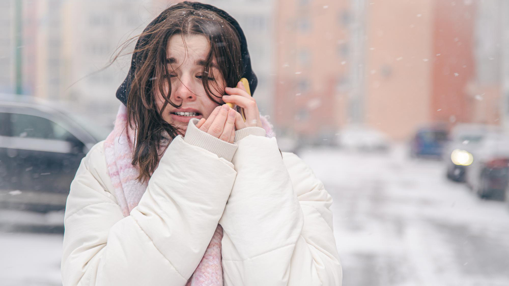 a woman walking in the cold with winter injuries crying on the phone