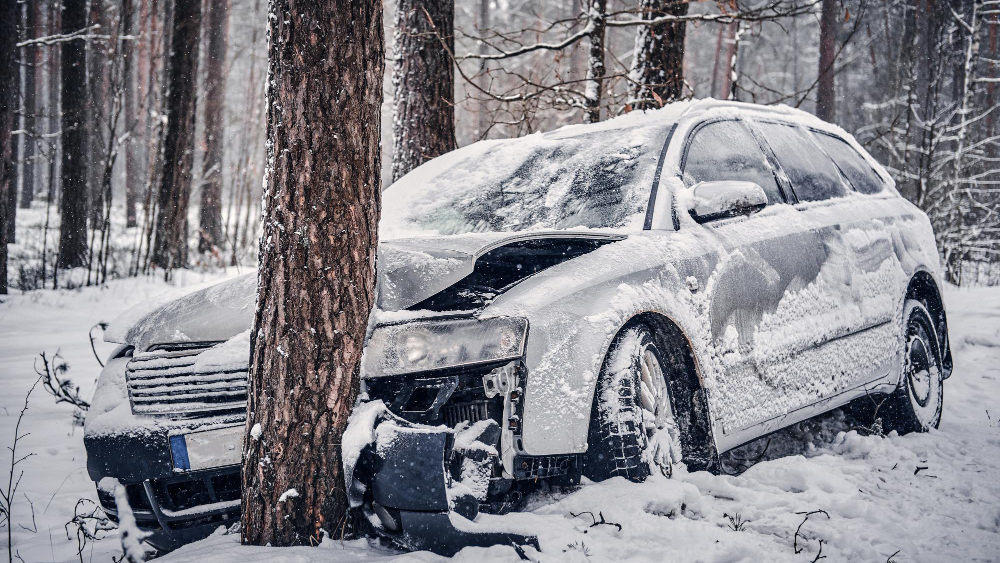 Snow-covered car crashed into a tree in a winter forest, illustrating a single-vehicle wreck where comparative negligence may be considered.