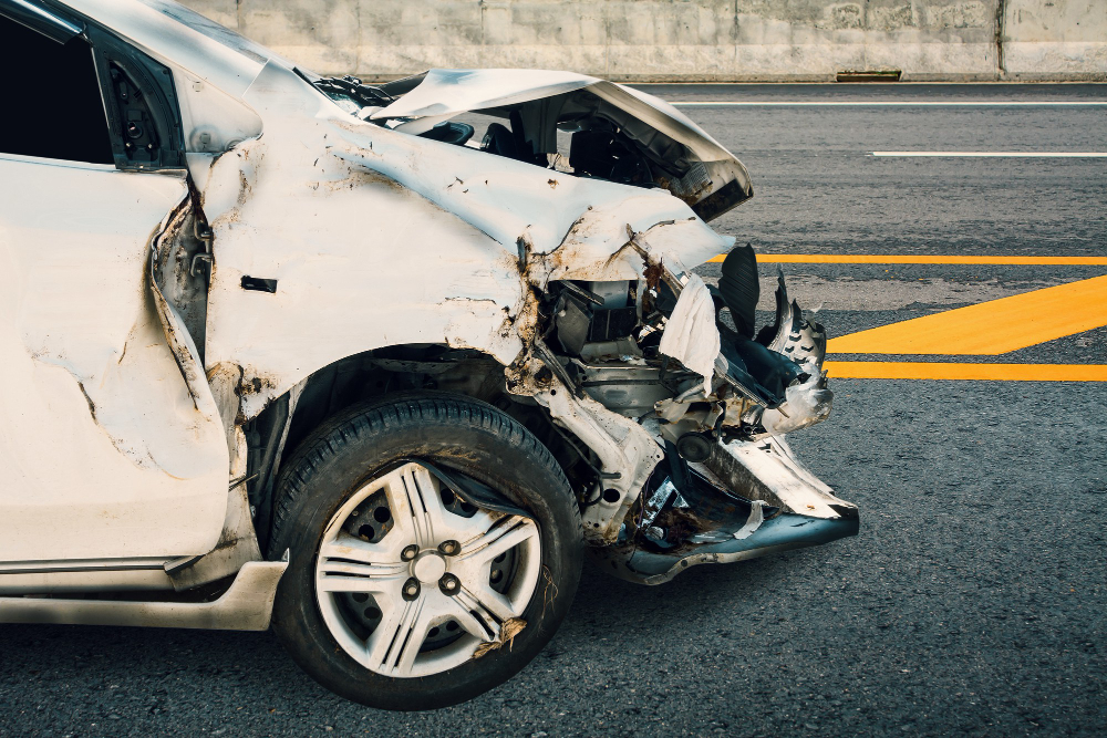 Severely damaged white car on the roadside after a collision, illustrating the aftermath of an uninsured driver accident with crumpled front-end damage.